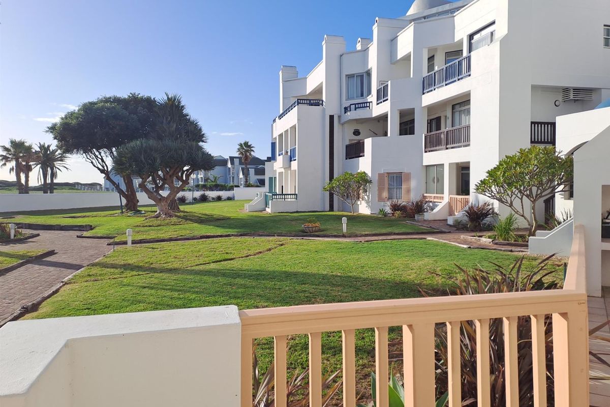 A view of the apartment complex exterior featuring white building facades, balconies, and well-maintained communal garden areas with paved walkways.
