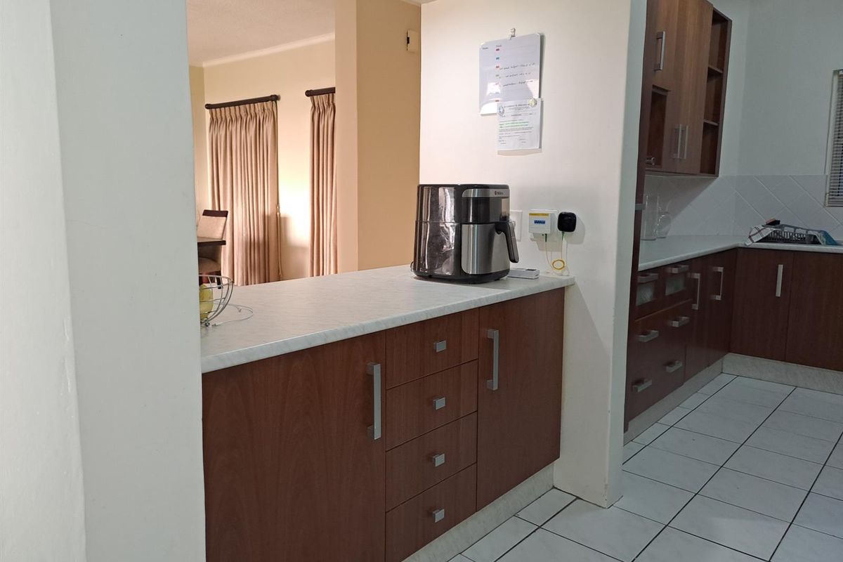 A functional kitchen featuring wood-finish cabinetry, laminate countertops, and tiled flooring, with an open-plan layout connecting to the adjacent living area.