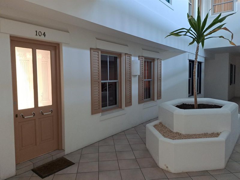 Entrance area of apartment 104 featuring a tiled walkway, decorative window shutters, and a central built-in planter box.