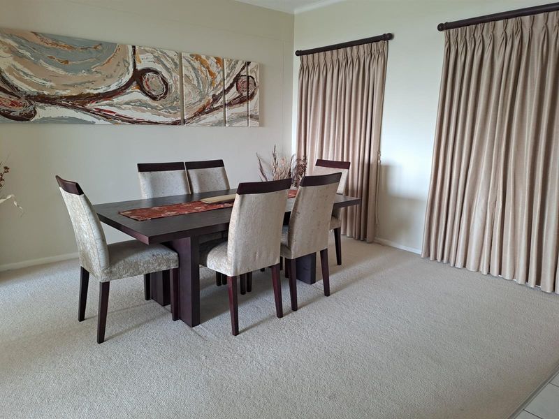 A dining room featuring neutral carpeting, wall-to-wall curtains, and a spacious layout suitable for formal dining.