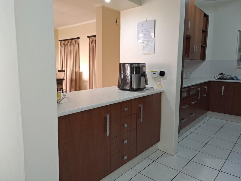 A functional kitchen featuring wood-finish cabinetry, laminate countertops, and tiled flooring, with an open-plan layout connecting to the adjacent living area.
