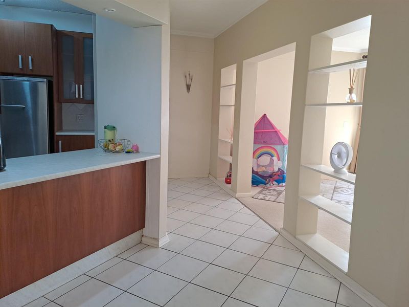 Open plan kitchen area featuring a breakfast bar, tiled flooring, and built-in shelving units leading into an adjacent living space.
