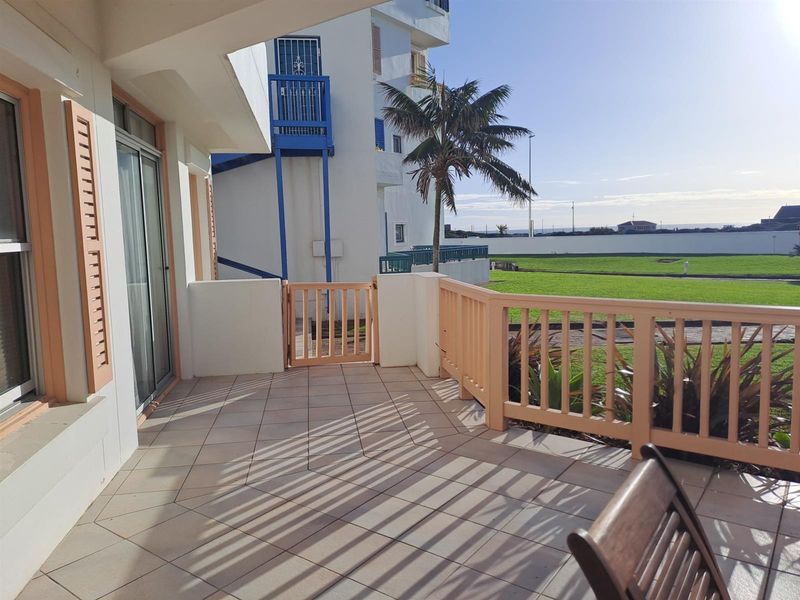 A covered patio area featuring tiled flooring and a wooden balustrade, offering direct access to the communal garden and outdoor space.