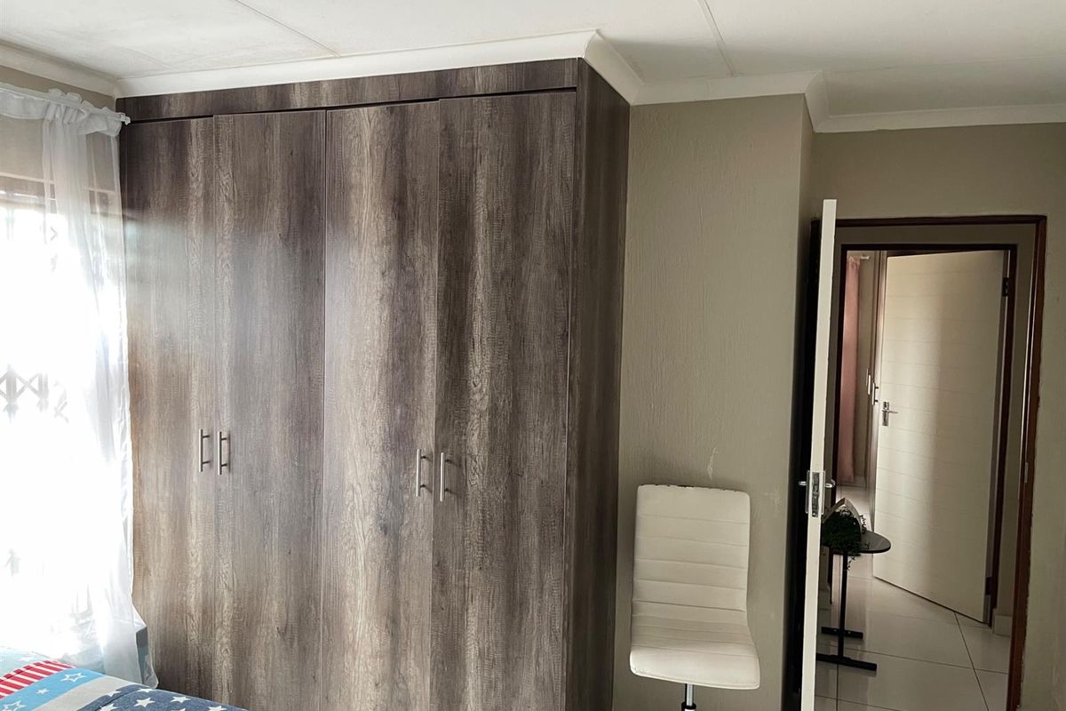 A bedroom featuring built-in wood-grain cabinetry and tiled flooring, with a doorway leading to an adjacent hallway.