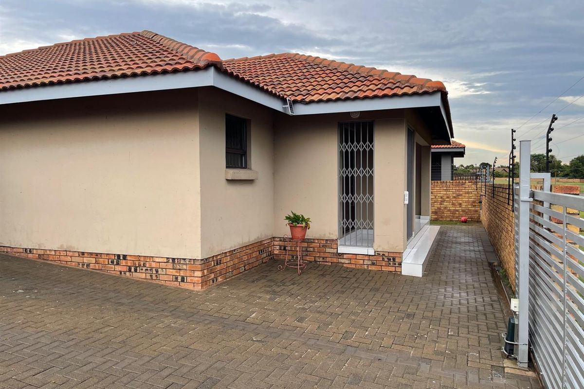 Side view of the house featuring a paved driveway, brick base detailing, tiled roof, and a security gate at the entrance.