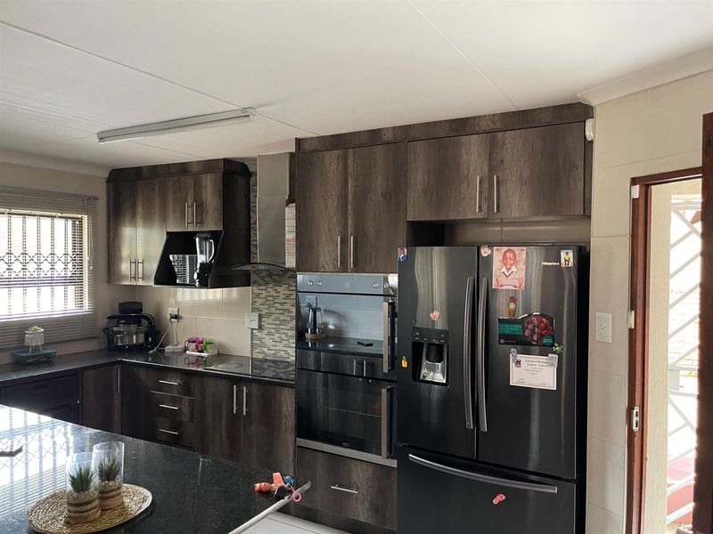 Modern kitchen featuring dark wood cabinetry, granite countertops, built-in oven, extractor fan, and a central island, offering a functional and stylish cooking space.