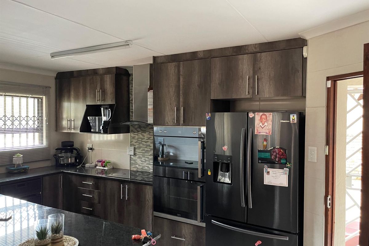 Modern kitchen featuring dark wood cabinetry, granite countertops, built-in oven, extractor fan, and a central island, offering a functional and stylish cooking space.