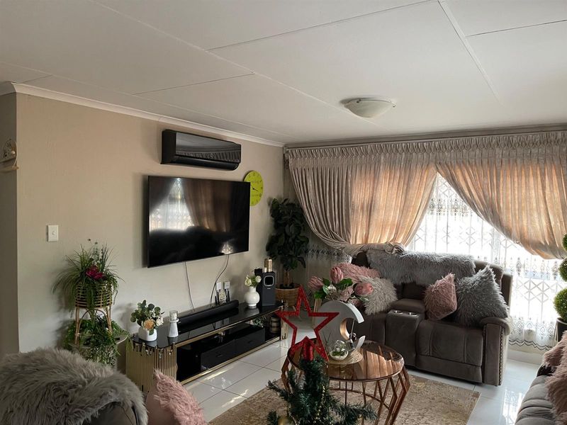 A comfortable living room featuring tiled flooring, a wall-mounted air conditioning unit, and large windows with draped curtains.