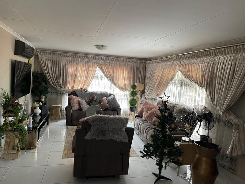 A comfortable living room featuring tiled flooring, large windows with heavy drapes, and a wall-mounted air conditioning unit.