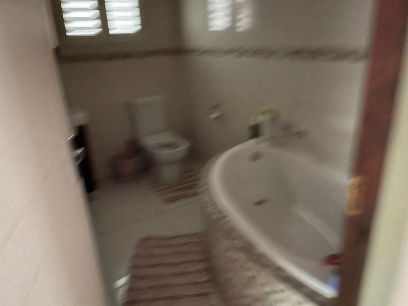A bathroom featuring a built-in bathtub, toilet, and tiled flooring with shuttered windows.