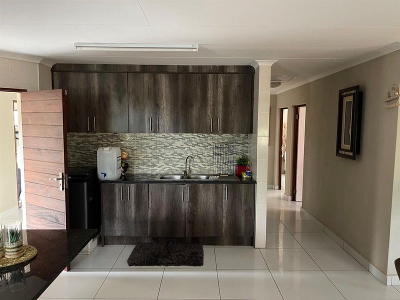 A functional kitchen area featuring dark wood-grain cabinetry, a mosaic tile backsplash, and a stainless steel double sink with tiled flooring.