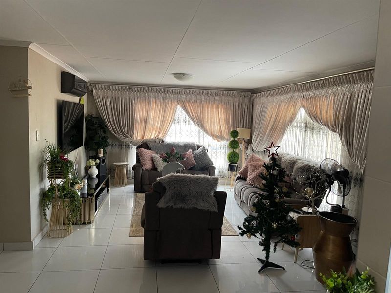 A well-maintained living room featuring large format floor tiles, wall-mounted air conditioning unit, and expansive windows with fitted curtain tracks.