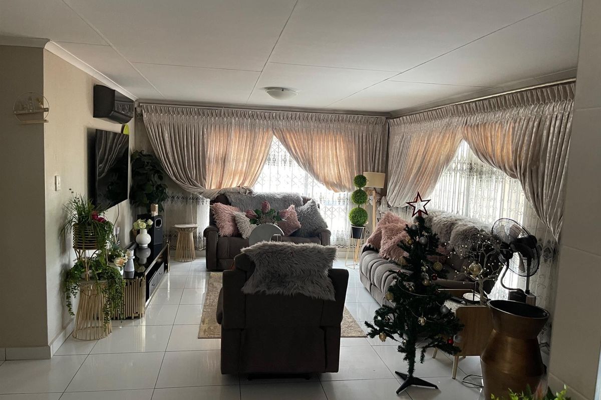 A well-maintained living room featuring large format floor tiles, wall-mounted air conditioning unit, and expansive windows with fitted curtain tracks.
