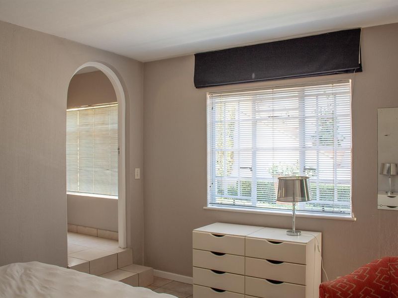 A bedroom featuring neutral wall tones, tiled flooring, an arched doorway leading to an adjacent space, and a window with fitted blinds.
