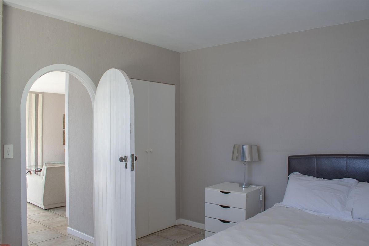 A bedroom featuring neutral wall tones, tiled flooring, a built-in wardrobe, and a distinctive arched doorway leading to an adjacent living space.