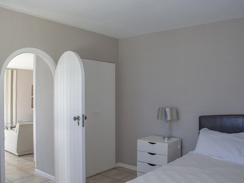 A bedroom featuring neutral wall tones, tiled flooring, a built-in wardrobe, and a distinctive arched doorway leading to an adjacent living space.