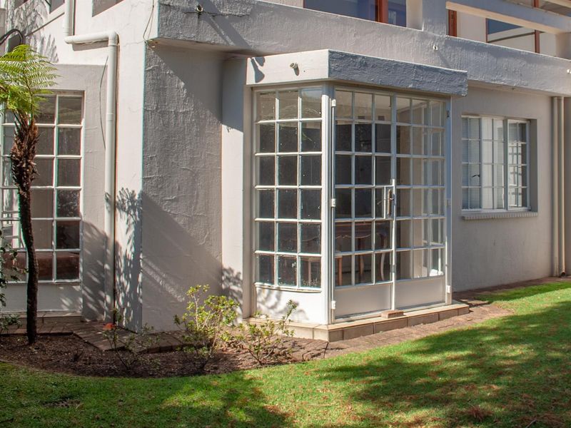 Rear exterior view of the property featuring an enclosed patio area with multi-pane glass doors and windows, set against a small garden.
