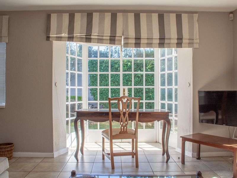 A bright living area featuring a large bay window with garden views, tiled flooring, and neutral wall finishes.