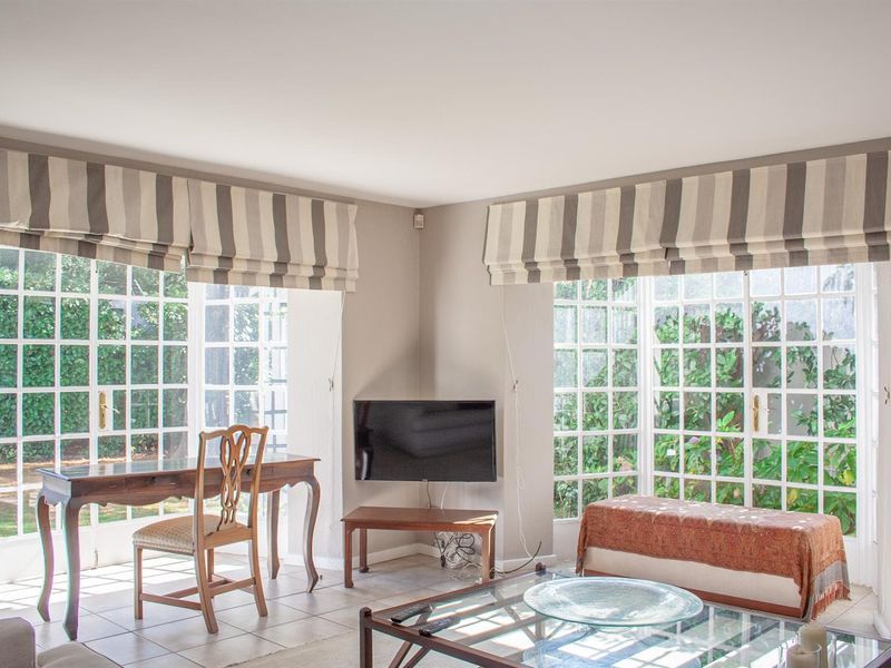 Bright living room featuring large corner windows, tiled flooring, and direct access to the garden through classic french doors.
