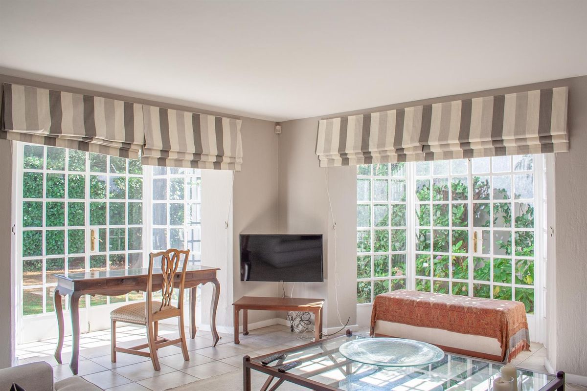 Bright living room featuring large corner windows, tiled flooring, and direct access to the garden through classic french doors.