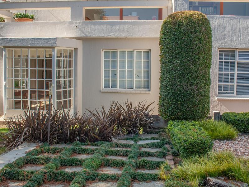 A well-maintained rear exterior view featuring a grid-patterned glass door, multi-pane windows, and a landscaped garden with a stone paver path.