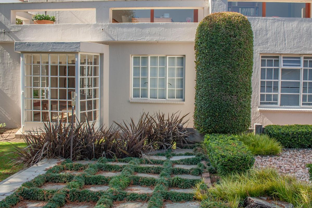 A well-maintained rear exterior view featuring a grid-patterned glass door, multi-pane windows, and a landscaped garden with a stone paver path.
