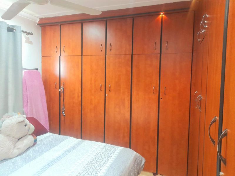 A bedroom featuring extensive floor-to-ceiling built-in wooden cupboards and a ceiling fan.