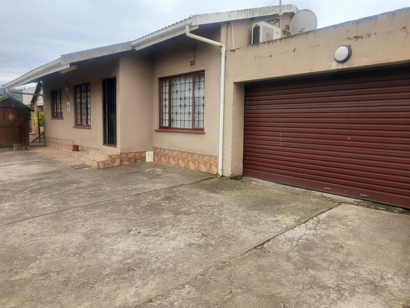 Front elevation of a single-story house featuring a roller shutter garage door, security window bars, and a concrete driveway.