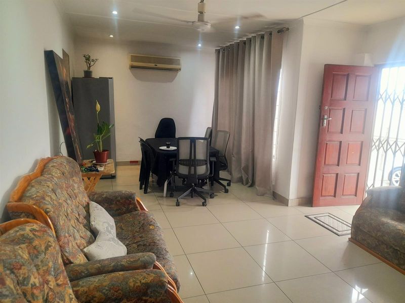 A living area featuring tiled flooring, recessed downlights, a ceiling fan, and a wall-mounted air conditioning unit, with direct access to the exterior.