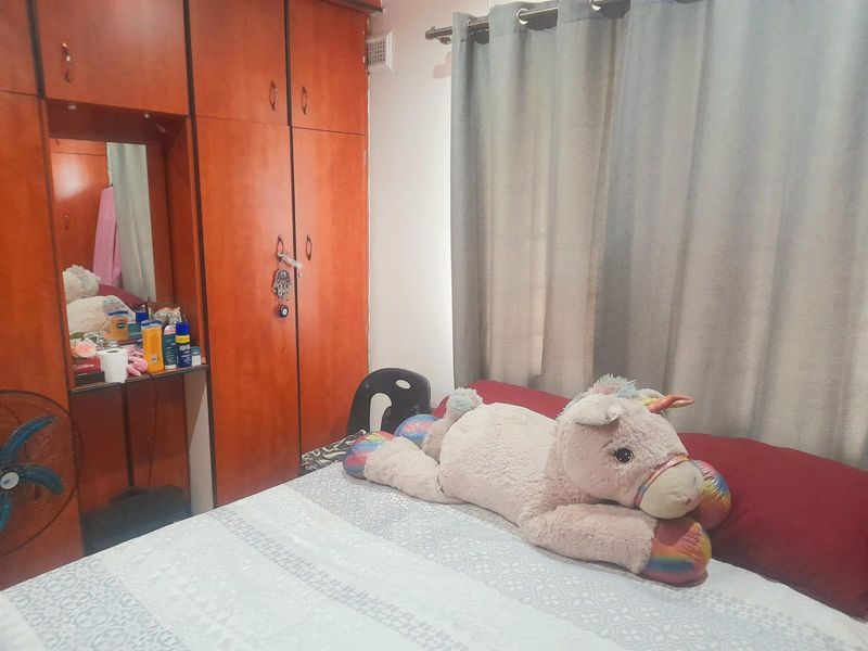 A bedroom featuring a large built-in wooden wardrobe with an integrated vanity mirror and neutral window curtains.