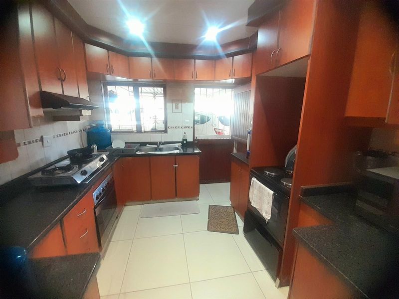 A functional kitchen featuring warm-toned built-in cabinetry, granite countertops, tiled flooring, and integrated cooking appliances, offering a practical layout for daily meal preparation.