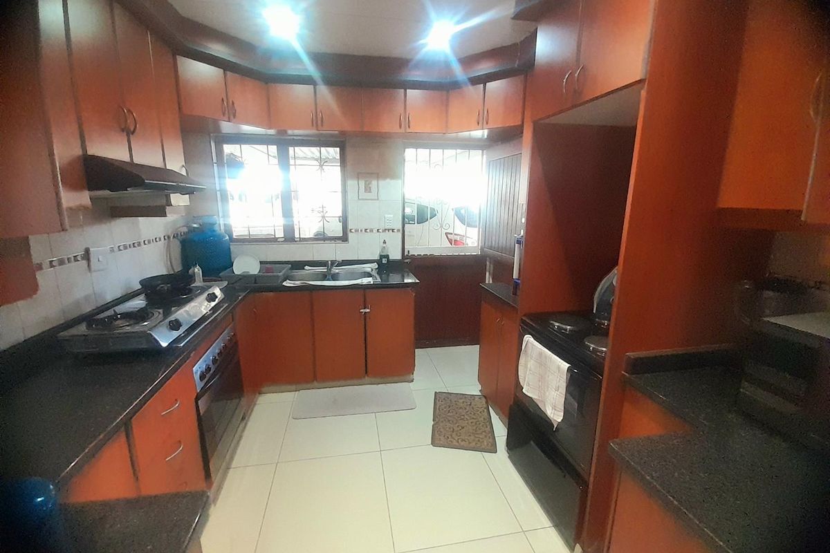 A functional kitchen featuring warm-toned built-in cabinetry, granite countertops, tiled flooring, and integrated cooking appliances, offering a practical layout for daily meal preparation.