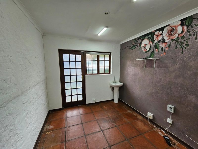 A utility space featuring terracotta floor tiles, a pedestal basin, and a glass-paneled exterior door with access to the outside.