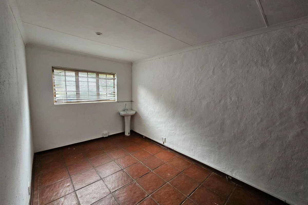 An empty room featuring terracotta floor tiles, a pedestal basin, and a window with fitted blinds.