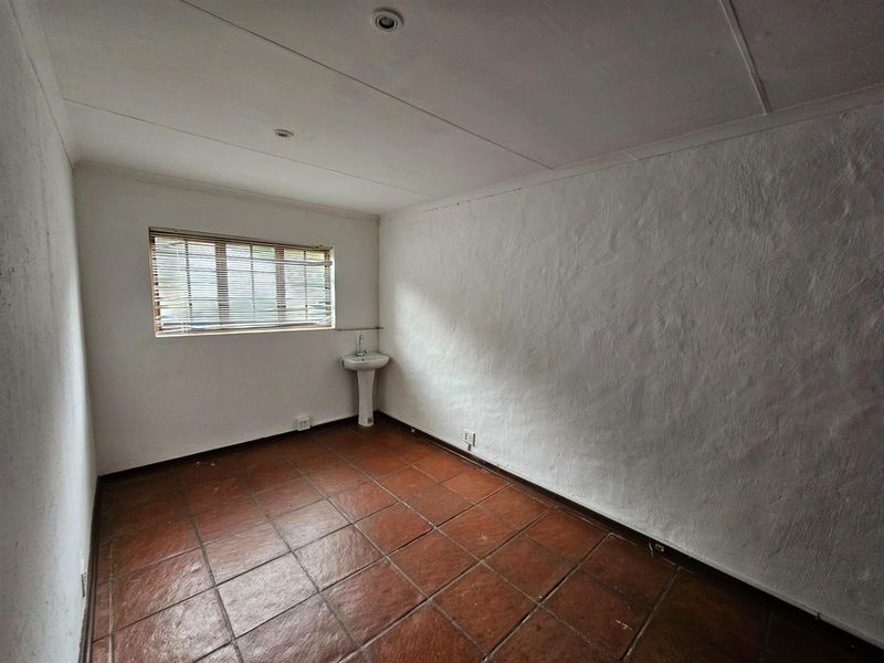 An empty room featuring terracotta floor tiles, a pedestal basin, and a window with fitted blinds.