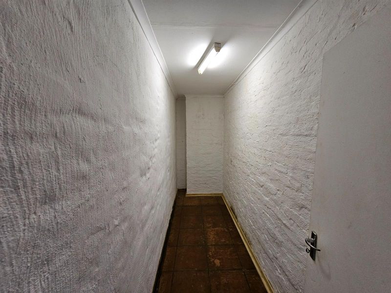 A narrow, utilitarian hallway featuring painted brick walls and tiled flooring, illuminated by a single overhead fluorescent light fixture.