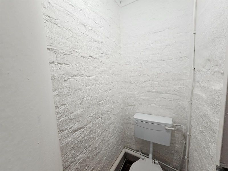 A compact, utilitarian bathroom featuring painted brick walls and a standard toilet suite with exposed plumbing.