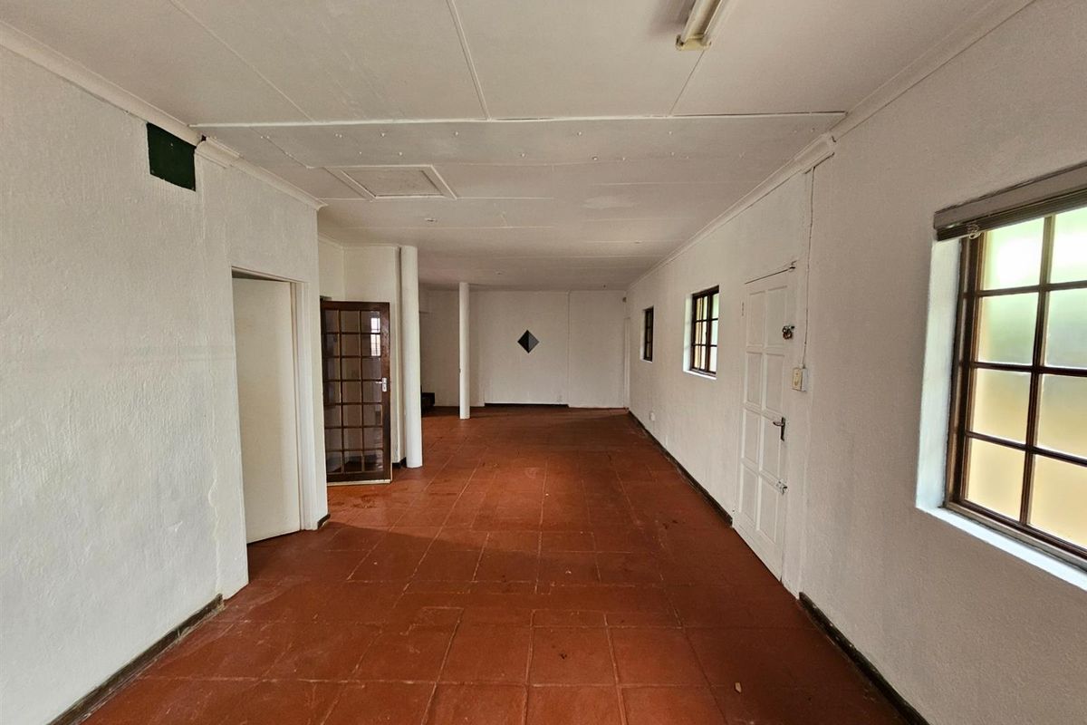 A spacious, empty interior room featuring terracotta-style floor tiles, multiple windows, and a neutral white finish, offering a blank canvas for renovation.