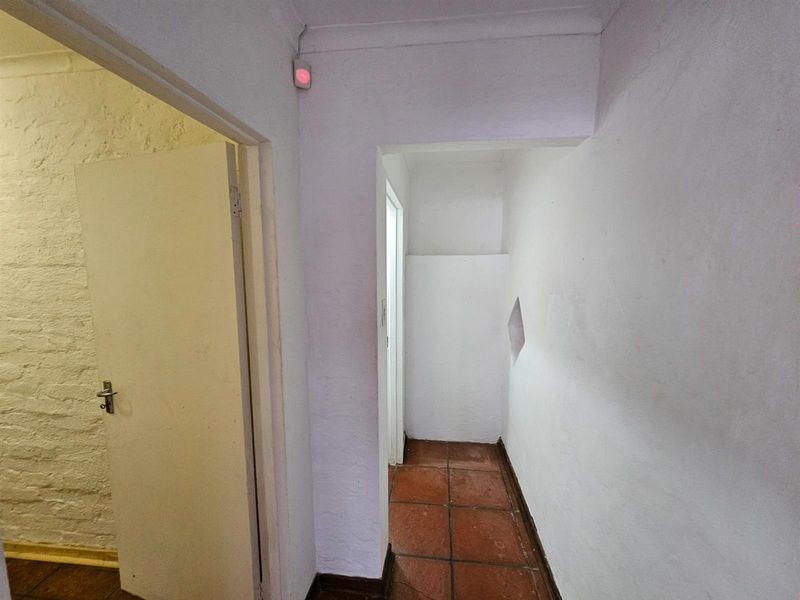 A narrow interior hallway featuring terracotta floor tiles and plain white walls, providing access to adjacent rooms.