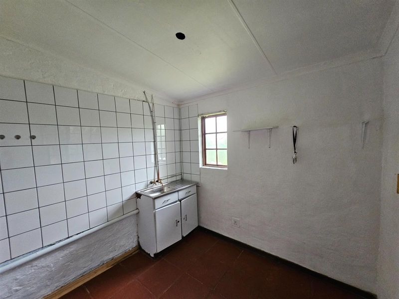 A functional laundry or utility space featuring a basic sink unit, tiled splashback, and terracotta-style flooring, suitable for renovation or modernization.