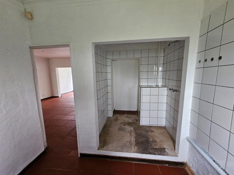 An interior view of a bathroom featuring a tiled shower area with exposed concrete flooring and an adjacent room with terracotta-style floor tiles.