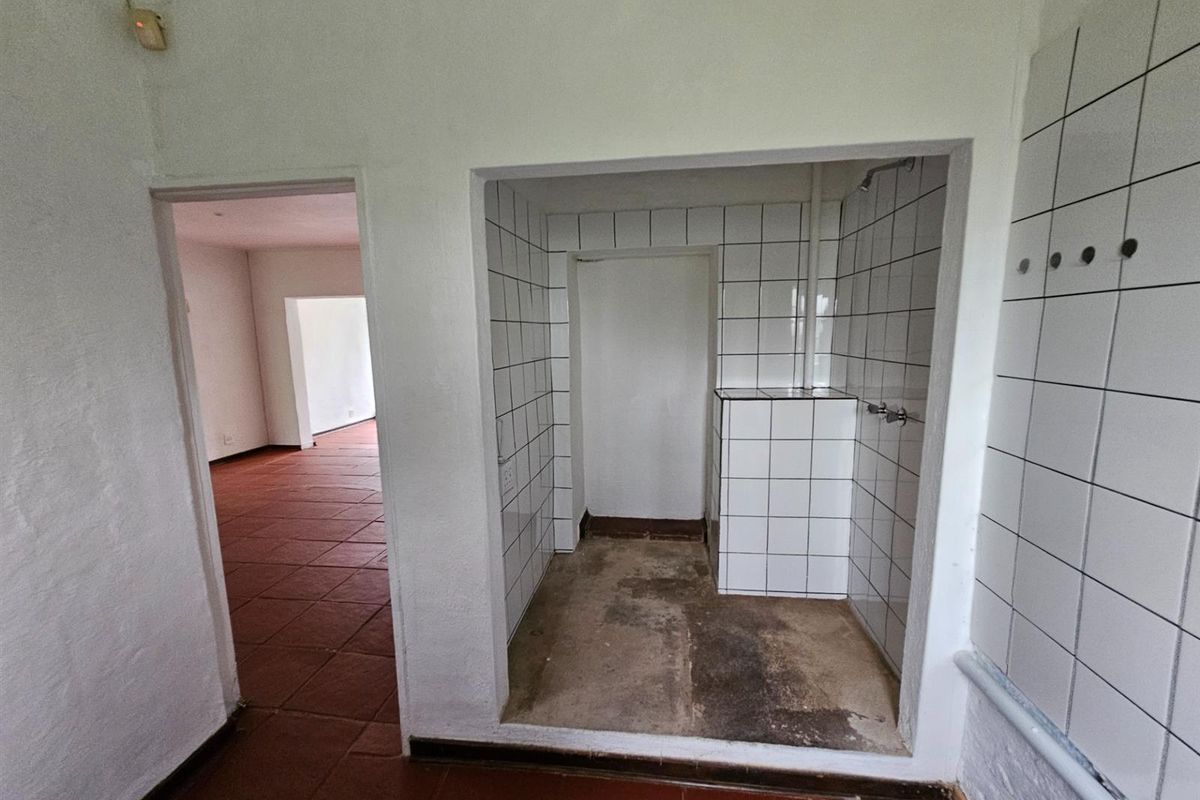 An interior view of a bathroom featuring a tiled shower area with exposed concrete flooring and an adjacent room with terracotta-style floor tiles.