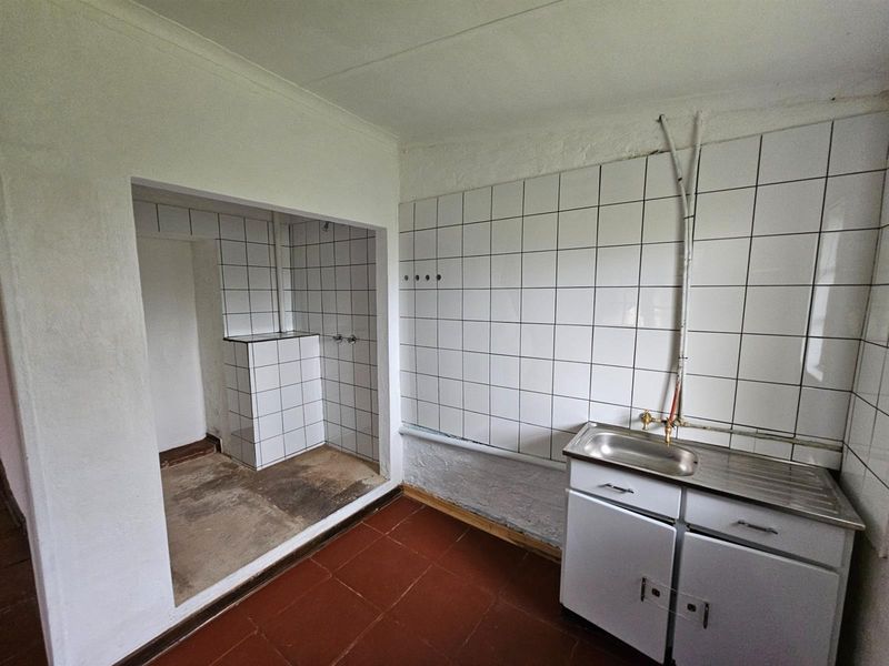 A utility or laundry area featuring a basic sink unit, tiled splashbacks, and an adjacent tiled alcove with exposed plumbing connections.