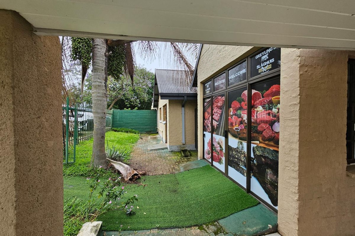 Exterior view of a commercial-style property entrance featuring large window decals, paved walkway, and artificial lawn area.