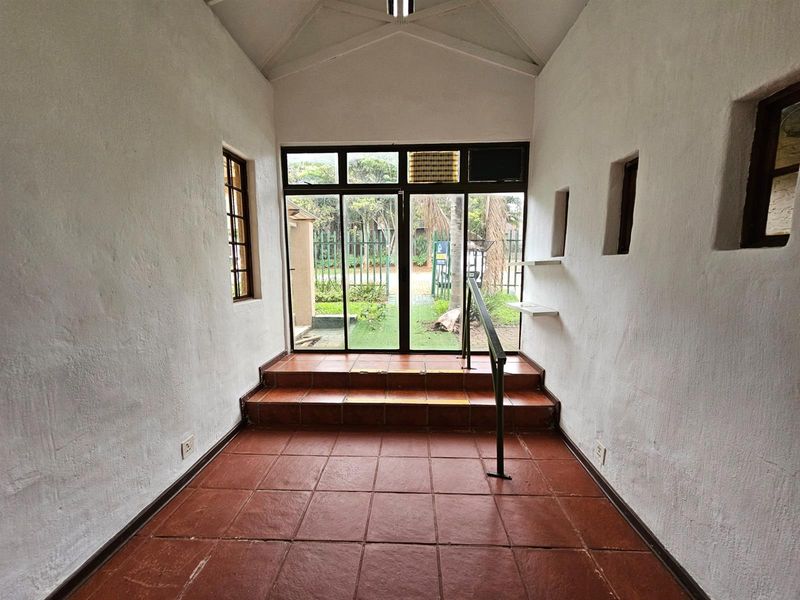 An entrance hall featuring terracotta tiled flooring, a vaulted ceiling, and a glass door providing direct access to the garden area.