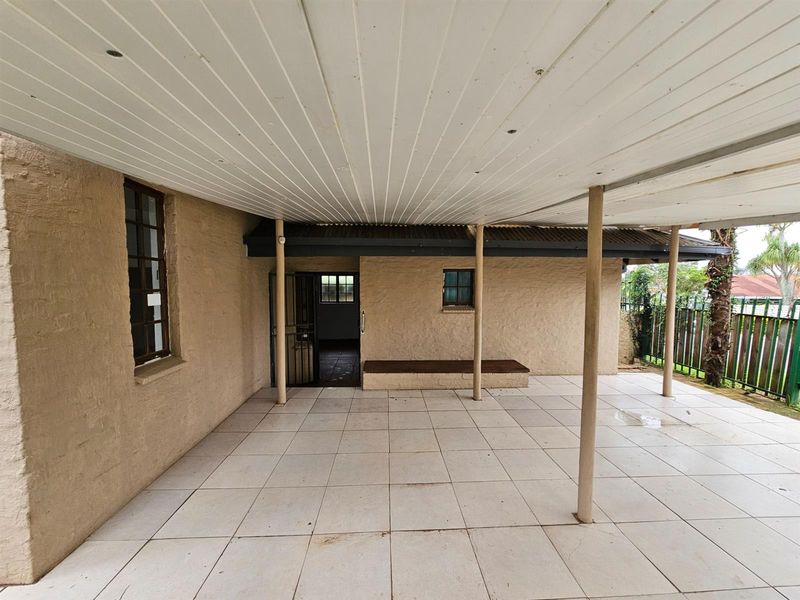 A covered patio area featuring tiled flooring, a white paneled ceiling, and a built-in bench, providing a functional outdoor space for relaxation.