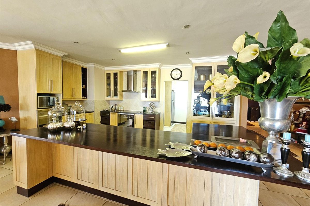 Spacious kitchen featuring light wood cabinetry, a large dark-toned breakfast bar, built-in oven, extractor fan, and integrated storage solutions.