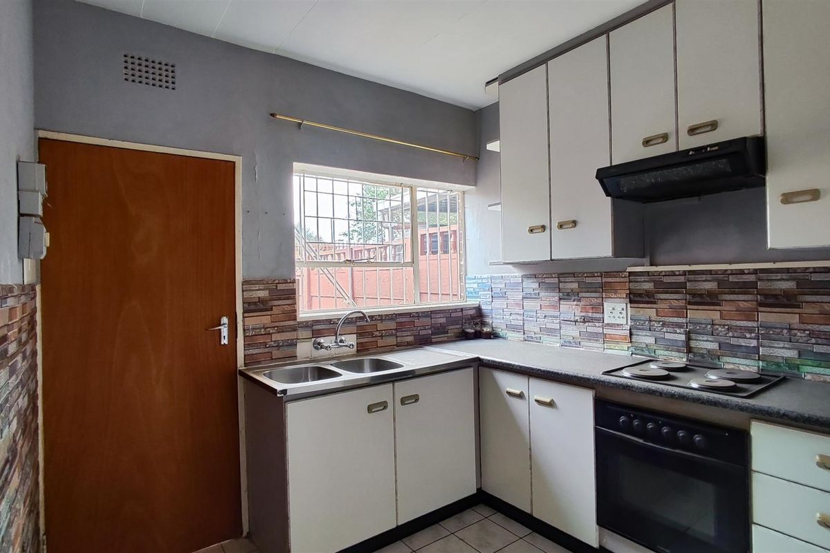 A functional kitchen featuring built-in cabinetry, a double sink, integrated oven and hob, and a tiled backsplash with a window for natural light.