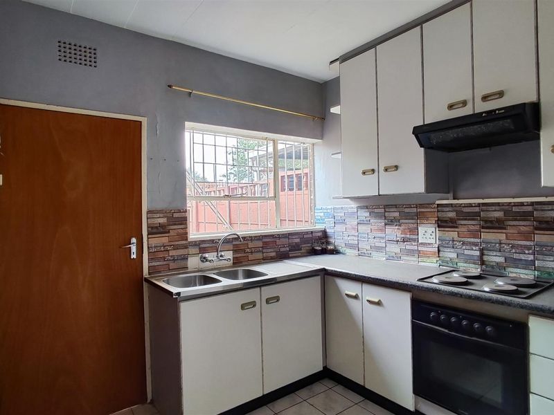 A functional kitchen featuring built-in cabinetry, a double sink, integrated oven and hob, and a tiled backsplash with a window for natural light.