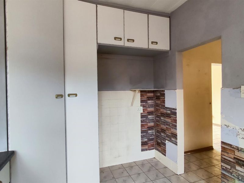 A functional kitchen area featuring built-in cabinetry, tiled flooring, and wall tiling, offering a blank canvas for potential renovation and modernization.